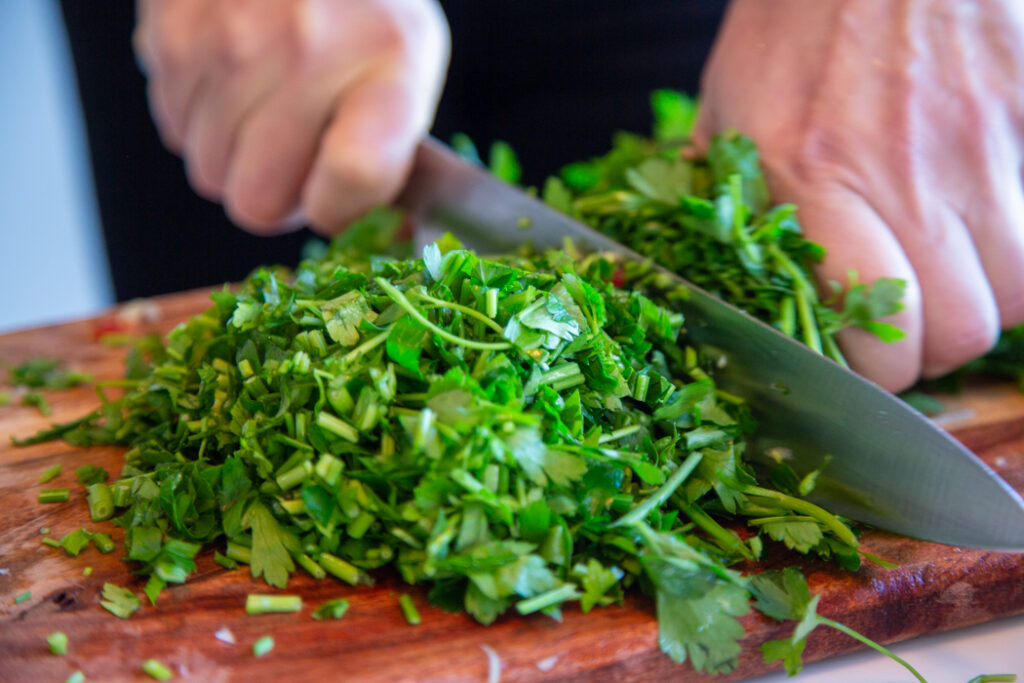 A person cutting up green vegetables on top of a wooden board.