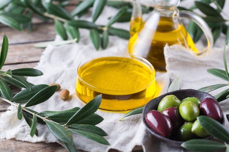 A bowl of olives next to olive oil and some leaves.