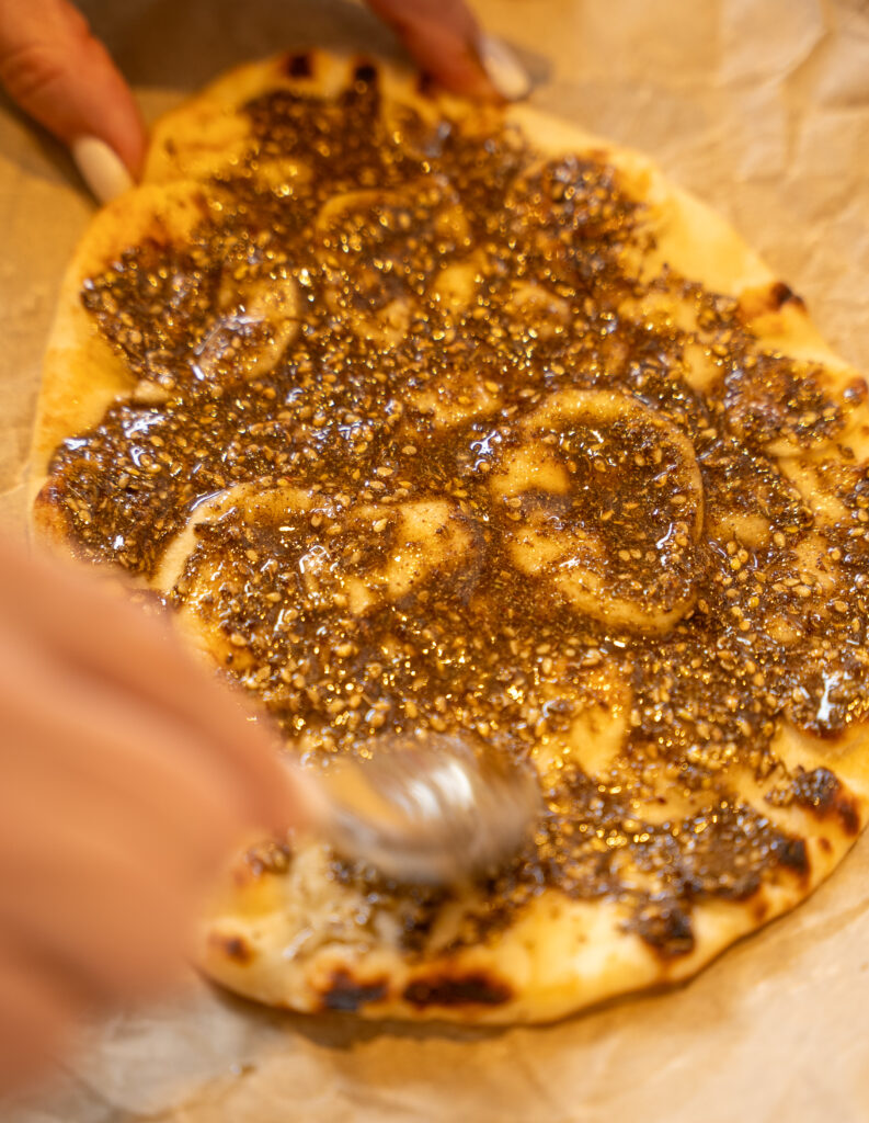 A person is using a spoon to sprinkle some sauce on the top of a pizza.