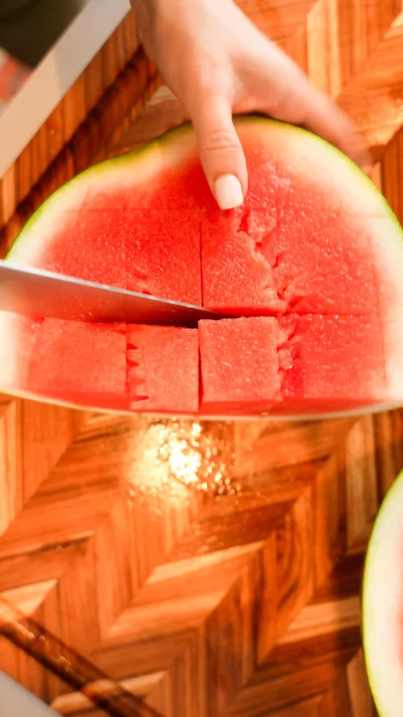 A woman holding up a watermelon in front of her face.