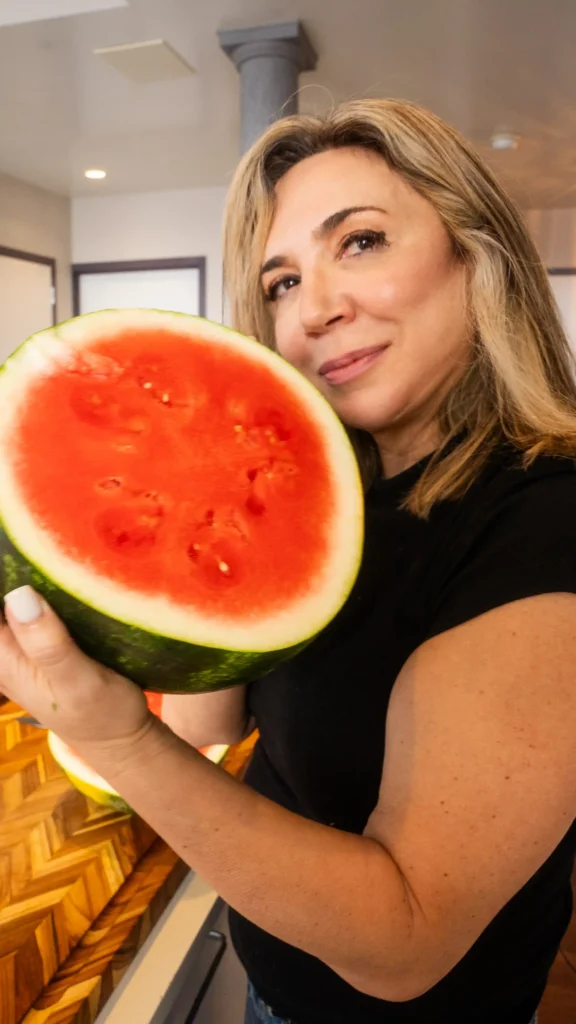 A woman holding up a watermelon in front of her face.