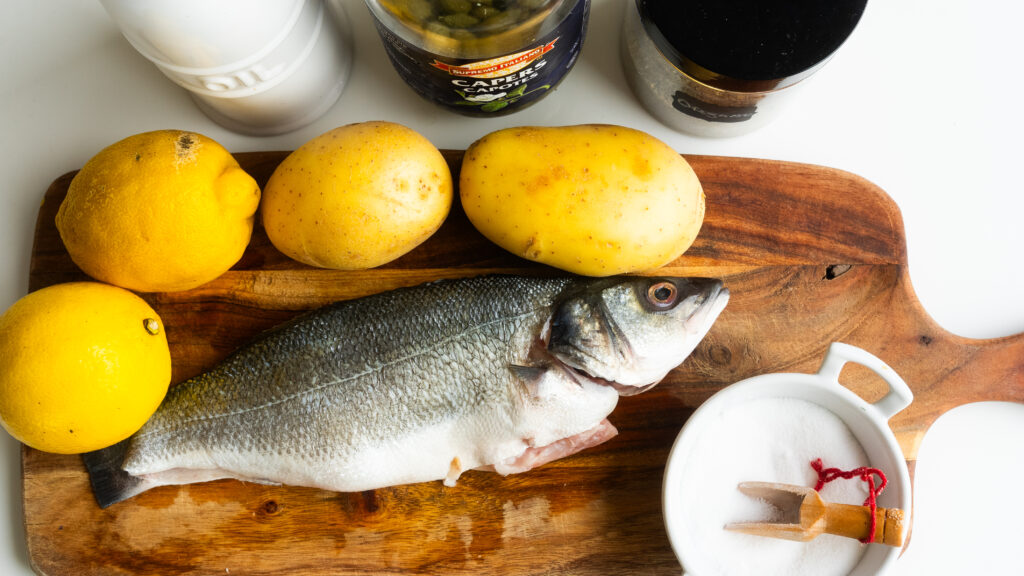 A fish is sitting on the table next to lemons.