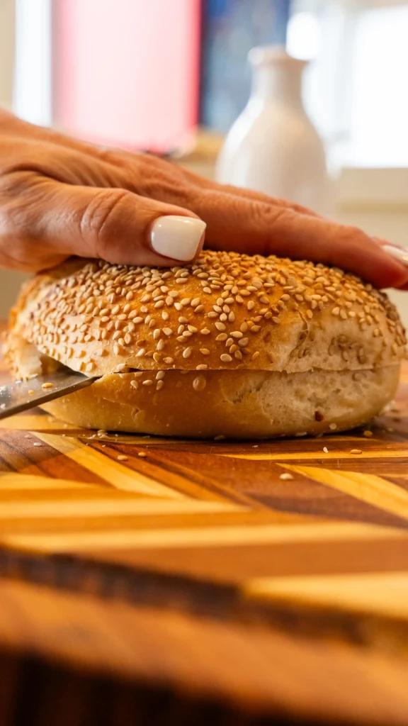 A bagel, avocado and other vegetables on a cutting board.