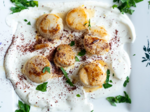 A plate of scallops with sauce and parsley.